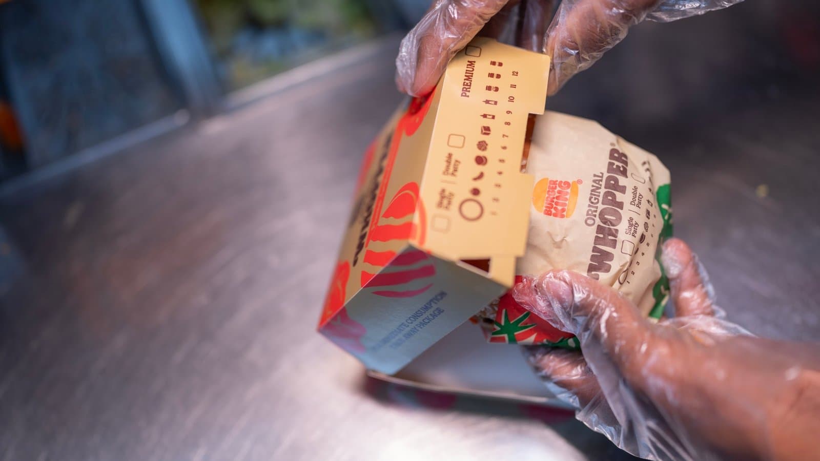A crew member in gloves packing an Original Whopper